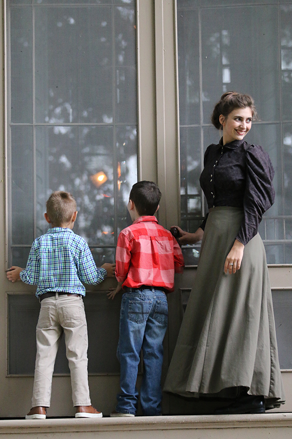 2 boys looking through a window and one woman looking behind them smiling broadly away from camera